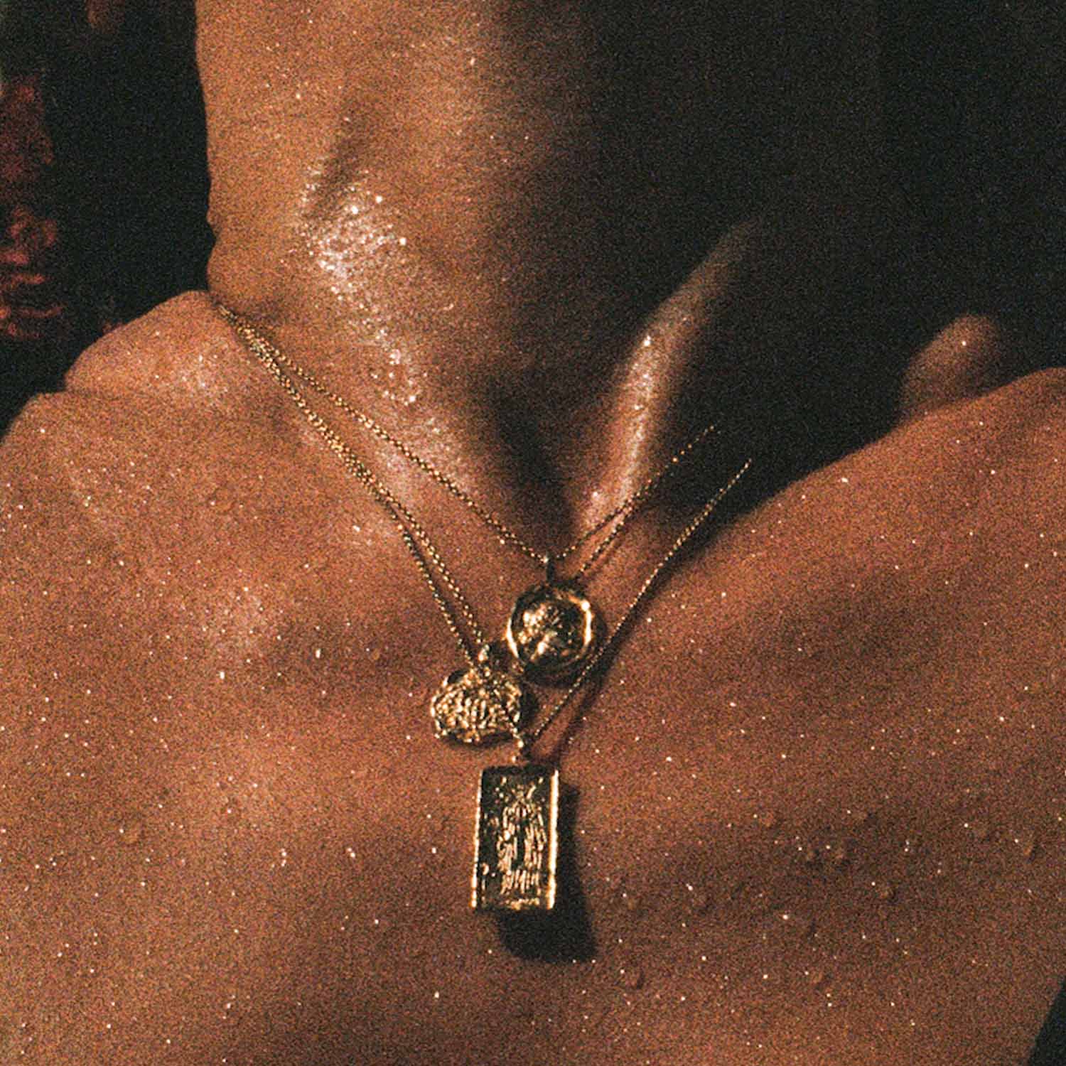 Close-up of a person wearing a gold necklace with two pendants on a dark background
